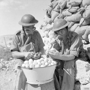 Soldiers peeling onions while wearing gas masks at Tobruk in October, 1941